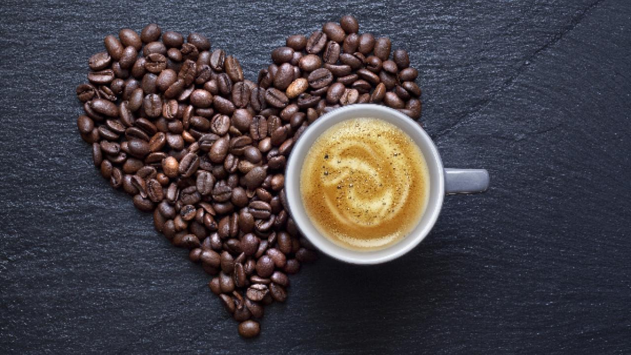 image of coffee beans in the shape of a heart, next to a brewed hot coffee drink with a swirly design in the foam